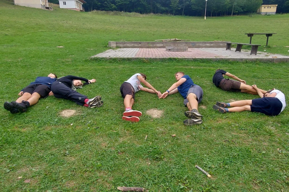 Účastníci sústredenia KMS ležiaci na tráve v tvare KMS
